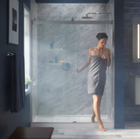 A woman steps out of a walk in shower with blue textured walls.