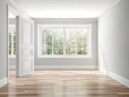 Empty room with wood floors, grey walls, and a large window looking out to trees